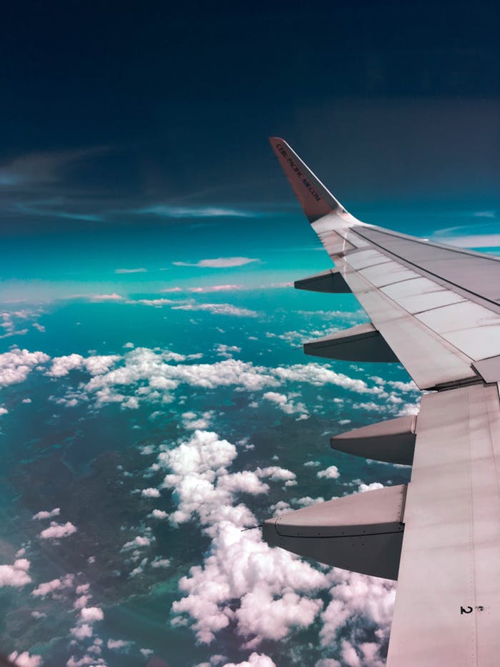 services-04 Aerial view of airplane wing over fluffy clouds with a deep turquoise sky.